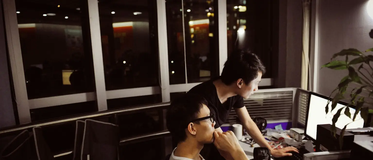 Two people working at computer monitors in a dark office at night